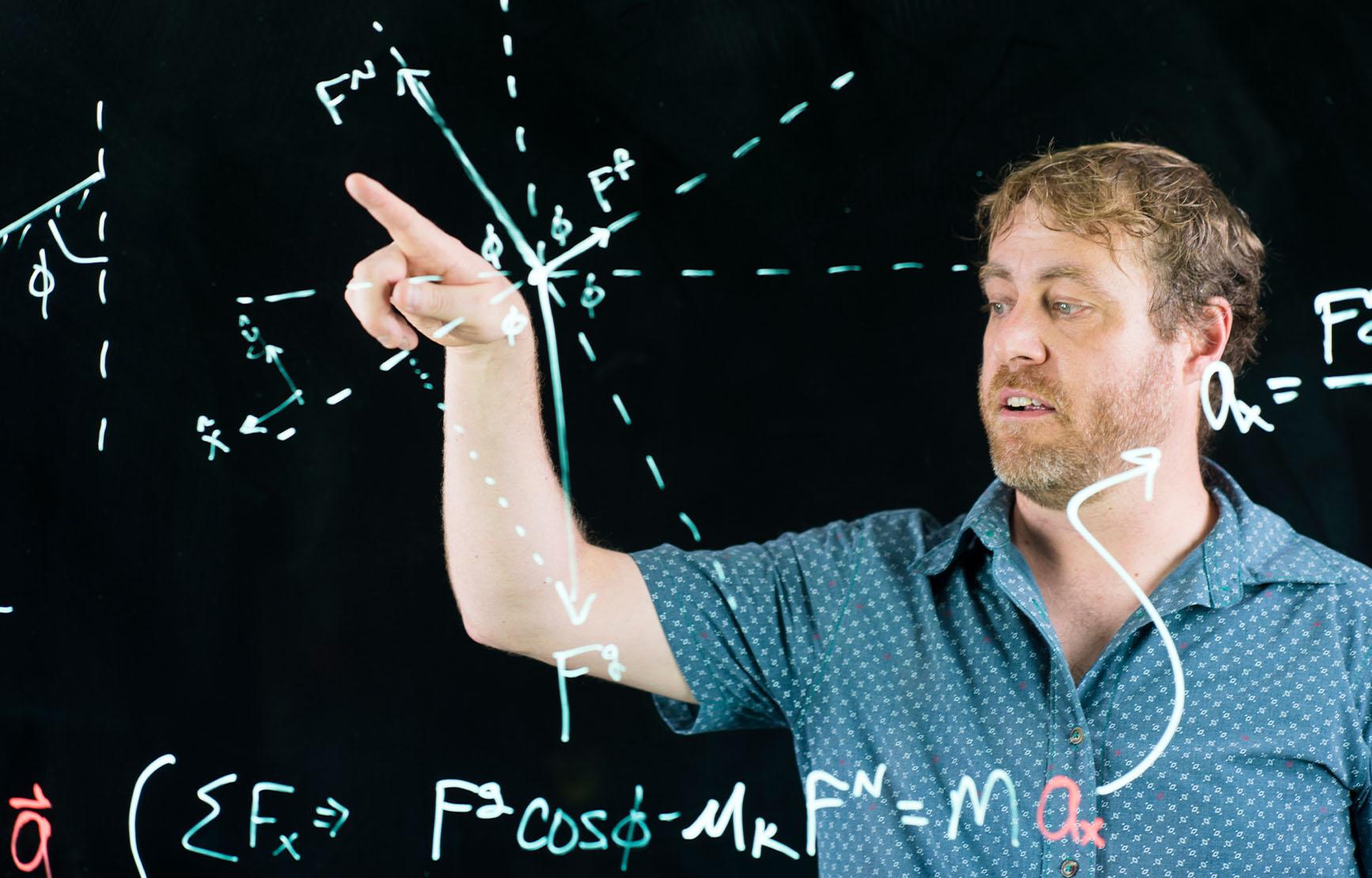 KC Walsh demonstrating physics equations and diagrams on a board